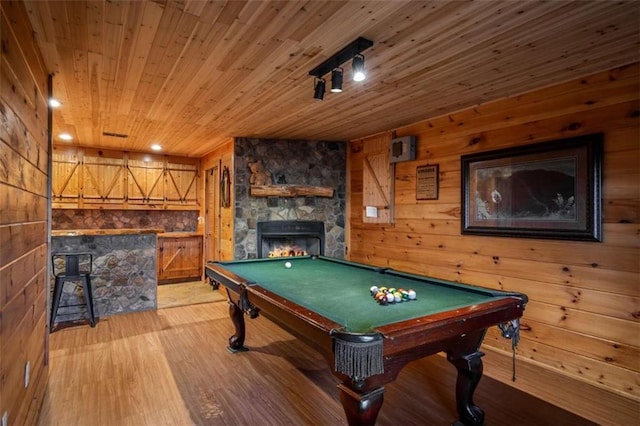 playroom with a stone fireplace, pool table, wood walls, wooden ceiling, and light wood-type flooring