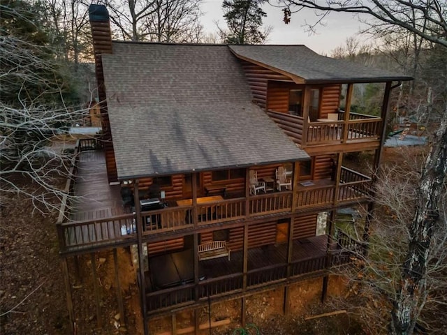 back of property with log veneer siding, roof with shingles, and a chimney