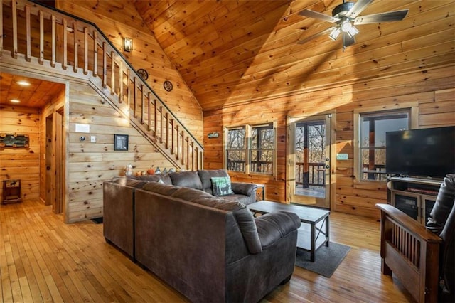 living room with stairway, wood-type flooring, wooden walls, and ceiling fan