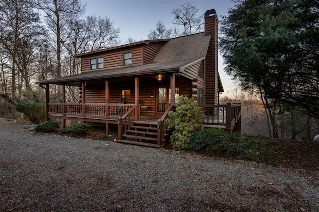 log cabin featuring log siding, covered porch, and a chimney