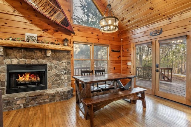 dining space featuring a stone fireplace, wood-type flooring, french doors, and wood walls