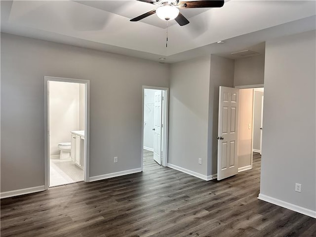 unfurnished bedroom with dark hardwood / wood-style flooring, a raised ceiling, ceiling fan, and ensuite bathroom