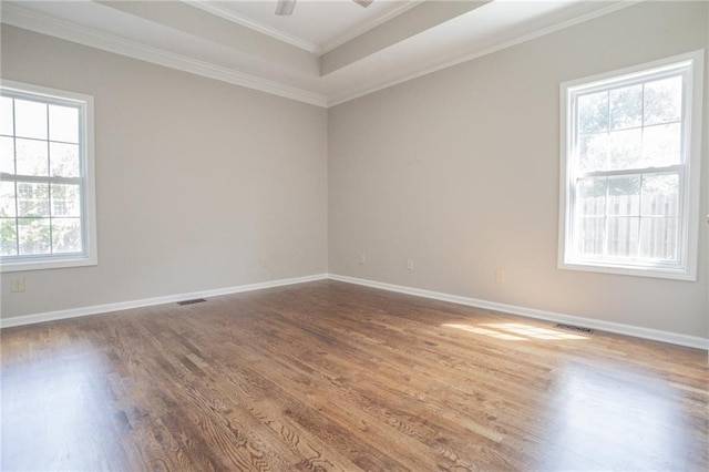 empty room featuring baseboards, visible vents, ornamental molding, and wood finished floors