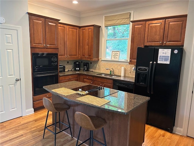 kitchen featuring decorative backsplash, light wood-type flooring, a sink, and black appliances