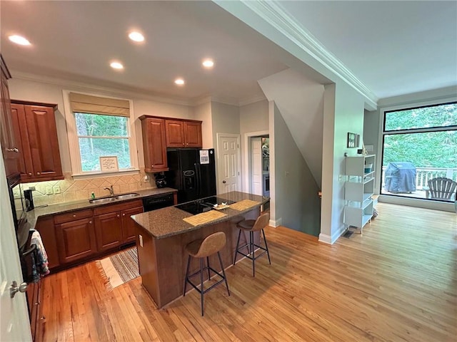 kitchen with a breakfast bar area, light wood finished floors, backsplash, a sink, and black appliances