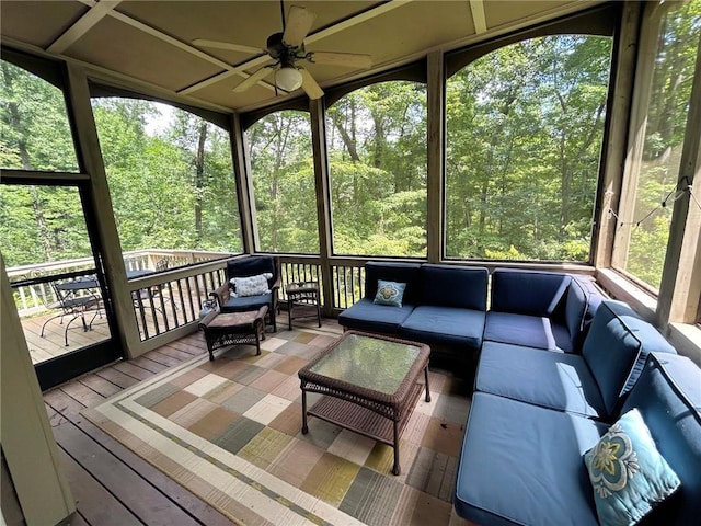 unfurnished sunroom featuring a forest view, a ceiling fan, and a healthy amount of sunlight