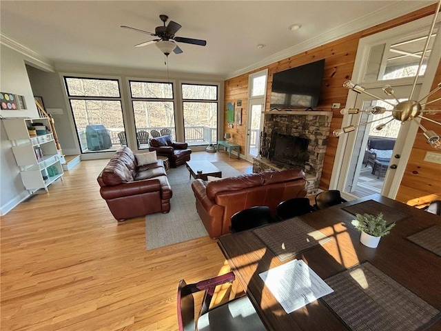 living room featuring crown molding, plenty of natural light, a stone fireplace, and light hardwood / wood-style flooring