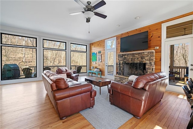 living area with a healthy amount of sunlight, light wood finished floors, ornamental molding, and a stone fireplace