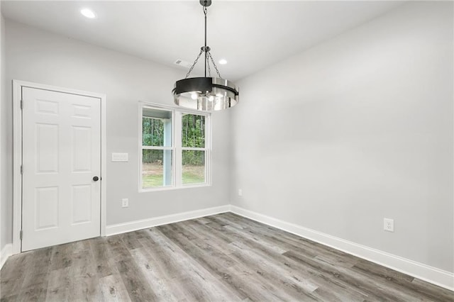 unfurnished dining area with a notable chandelier, recessed lighting, wood finished floors, and baseboards