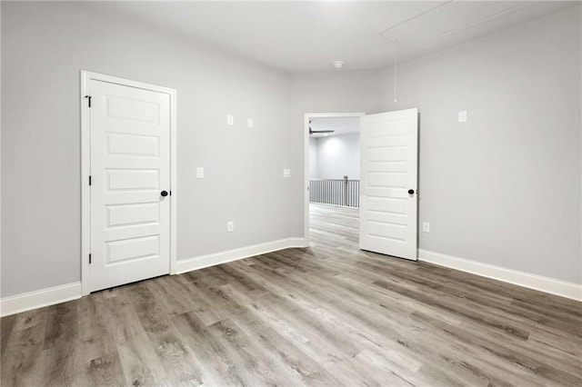 unfurnished room featuring attic access, baseboards, and wood finished floors