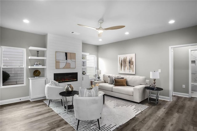 living room with a fireplace, visible vents, a ceiling fan, wood finished floors, and baseboards