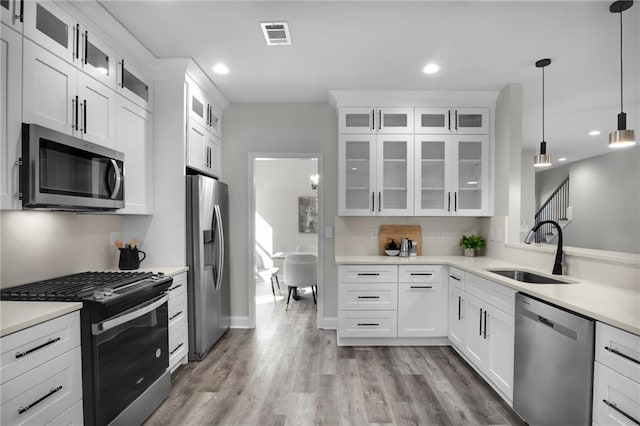 kitchen with stainless steel appliances, light countertops, visible vents, light wood-style floors, and a sink