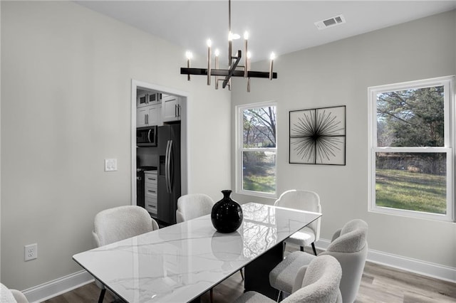 dining area with a notable chandelier, baseboards, visible vents, and wood finished floors