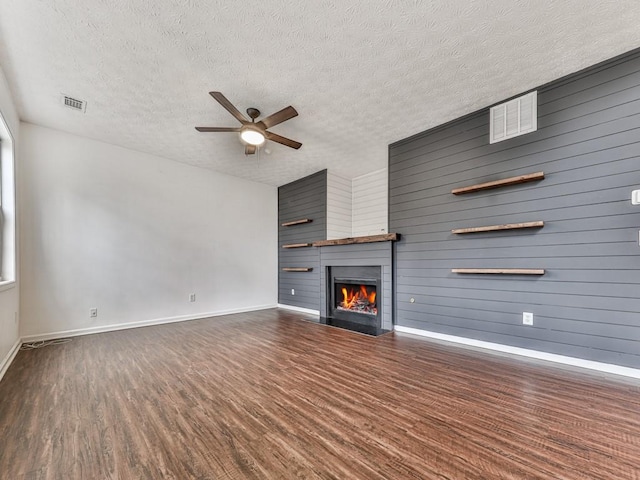 unfurnished living room with dark hardwood / wood-style flooring, a textured ceiling, a large fireplace, and ceiling fan