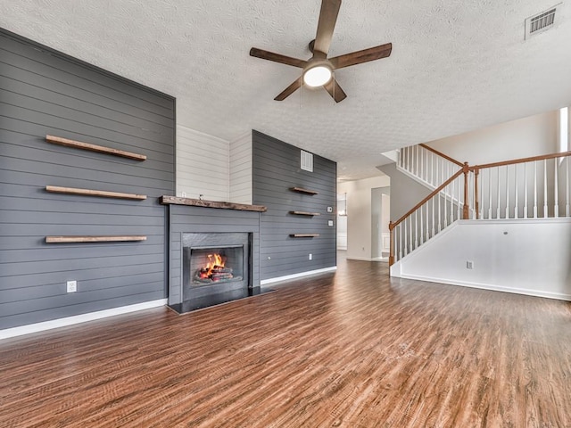 unfurnished living room with a textured ceiling, dark hardwood / wood-style floors, ceiling fan, and wood walls