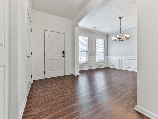 foyer entrance with a textured ceiling, dark hardwood / wood-style floors, an inviting chandelier, and crown molding