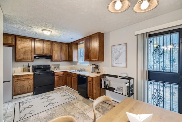 kitchen with brown cabinets, under cabinet range hood, light countertops, black appliances, and a sink