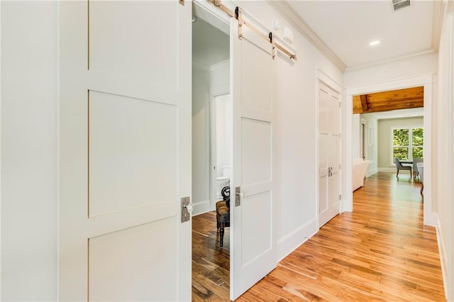 hallway featuring crown molding, a barn door, and light hardwood / wood-style flooring