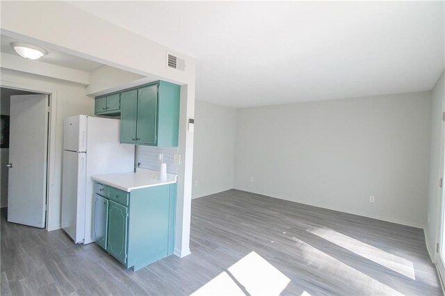 kitchen featuring green cabinetry, white refrigerator, wood-type flooring, and tasteful backsplash