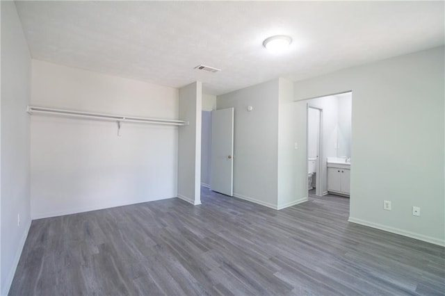 unfurnished bedroom with ensuite bathroom, a closet, and dark hardwood / wood-style floors