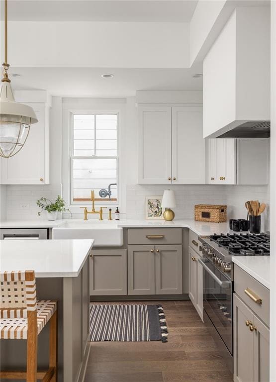 kitchen with gray cabinets, high end stove, sink, hanging light fixtures, and wall chimney range hood