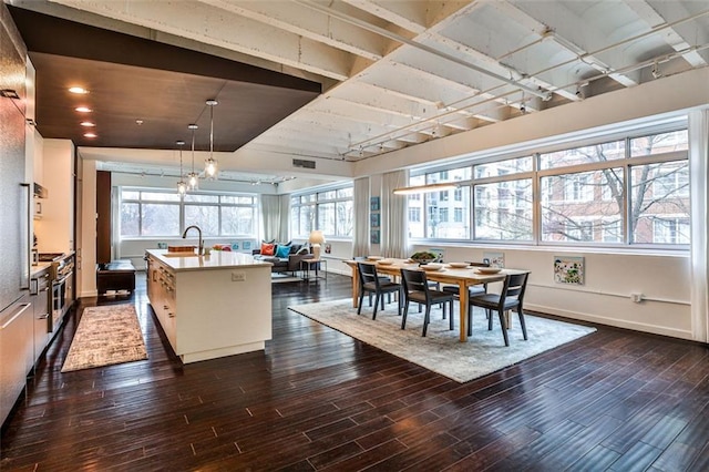 kitchen with dark wood-type flooring, a center island with sink, and decorative light fixtures