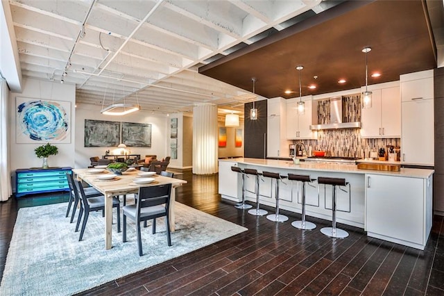 kitchen with wall chimney exhaust hood, decorative light fixtures, dark hardwood / wood-style flooring, decorative backsplash, and white cabinets