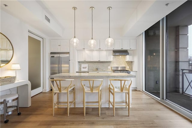 kitchen with white cabinetry, wall chimney range hood, a kitchen breakfast bar, and built in refrigerator