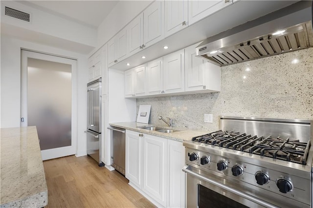 kitchen featuring sink, white cabinets, premium appliances, light stone counters, and wall chimney exhaust hood