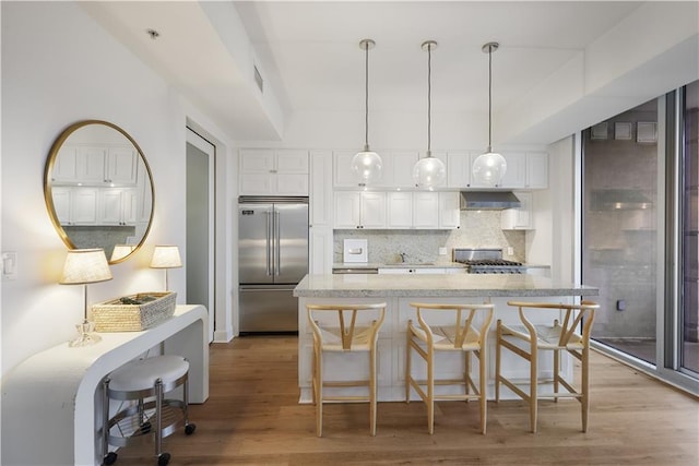 kitchen with pendant lighting, wall chimney range hood, white cabinetry, stove, and stainless steel built in refrigerator