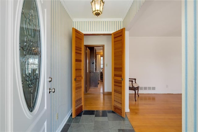 foyer with wallpapered walls, baseboards, visible vents, and crown molding