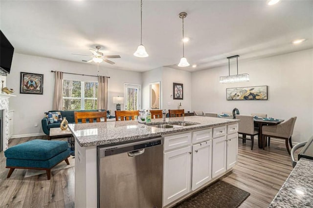 kitchen with white cabinets, a kitchen island with sink, dishwasher, a sink, and hanging light fixtures