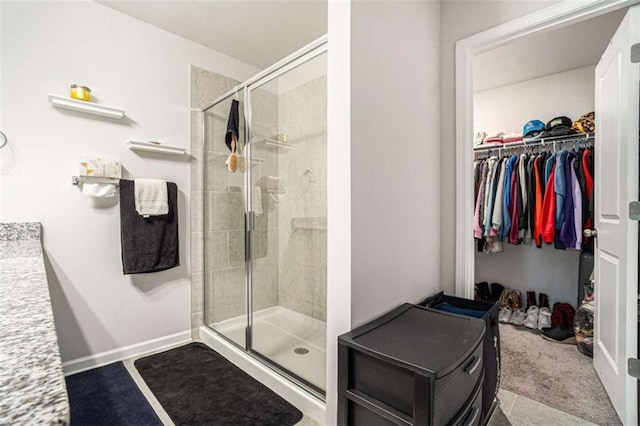bathroom featuring a spacious closet, baseboards, and a stall shower