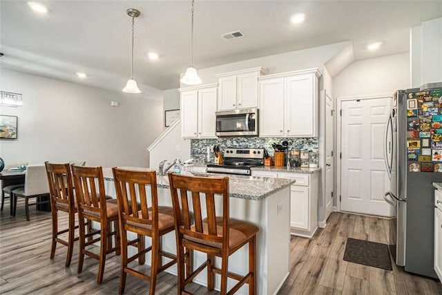 kitchen with a kitchen breakfast bar, white cabinetry, appliances with stainless steel finishes, wood finished floors, and backsplash