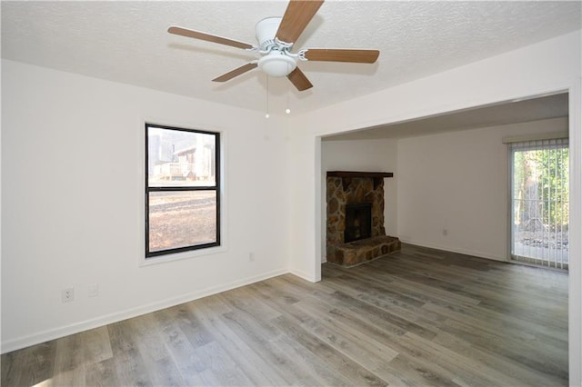 unfurnished living room featuring a ceiling fan, a stone fireplace, a textured ceiling, wood finished floors, and baseboards