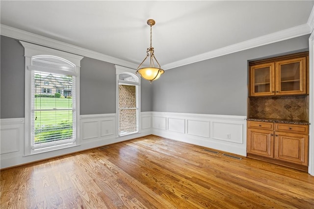 unfurnished dining area with wainscoting, ornamental molding, and light wood-style flooring