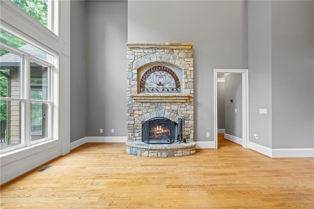 unfurnished living room featuring a fireplace, wood finished floors, baseboards, and a towering ceiling