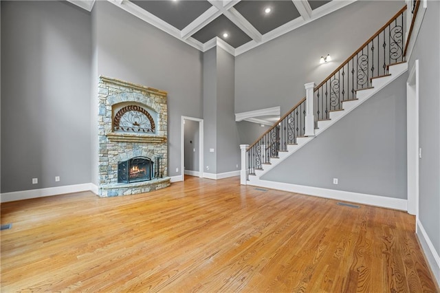 unfurnished living room featuring baseboards, a towering ceiling, coffered ceiling, stairway, and beamed ceiling