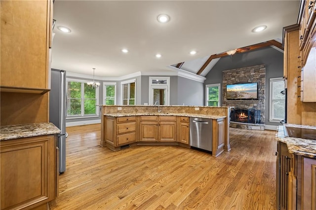 kitchen with stainless steel appliances, light wood finished floors, a stone fireplace, a chandelier, and light stone countertops