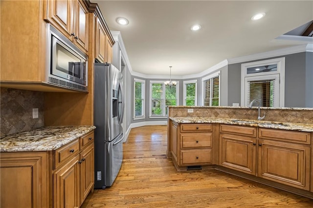 kitchen featuring appliances with stainless steel finishes, a sink, ornamental molding, brown cabinetry, and light wood-style floors