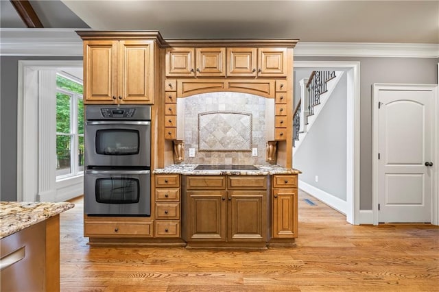kitchen with stainless steel double oven, crown molding, black electric stovetop, light stone countertops, and light wood-style floors