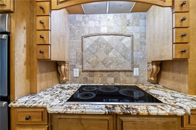 kitchen featuring black electric cooktop, brown cabinetry, light stone counters, and backsplash