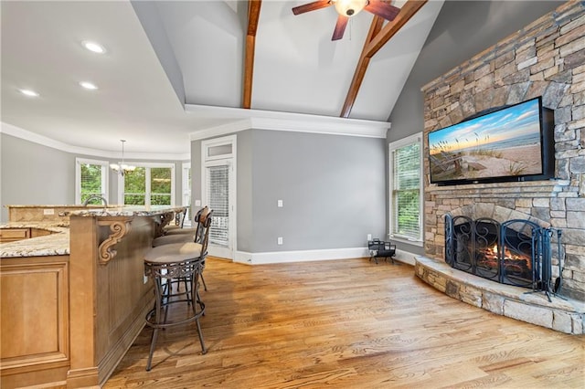 living room with a stone fireplace, light wood finished floors, a ceiling fan, baseboards, and crown molding