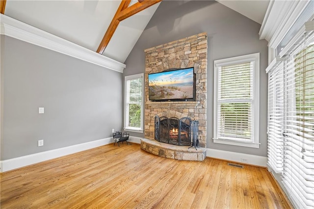 unfurnished living room with a stone fireplace, baseboards, wood finished floors, vaulted ceiling, and plenty of natural light
