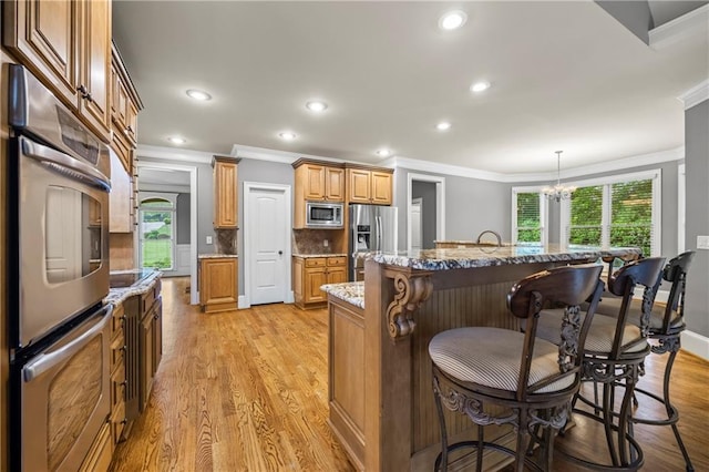 kitchen featuring stainless steel appliances, crown molding, a kitchen bar, healthy amount of natural light, and light wood-style floors