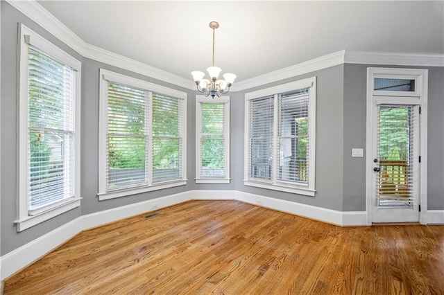 unfurnished dining area featuring a chandelier, baseboards, plenty of natural light, wood finished floors, and crown molding