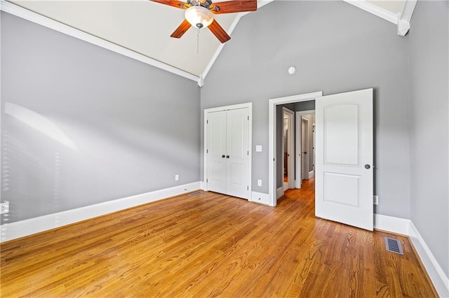 unfurnished bedroom featuring high vaulted ceiling, wood finished floors, baseboards, a closet, and ceiling fan