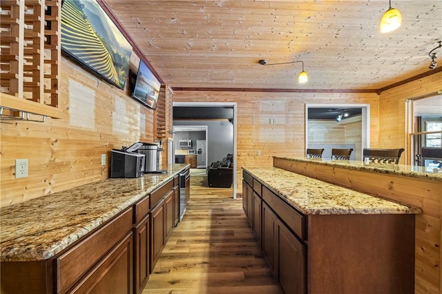 kitchen with wood walls, wood finished floors, wood ceiling, light stone countertops, and decorative light fixtures