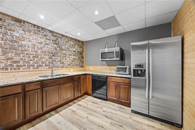 kitchen with appliances with stainless steel finishes, a sink, a drop ceiling, light wood-style flooring, and brick wall