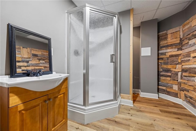full bath featuring a shower stall, baseboards, wood finished floors, vanity, and a paneled ceiling